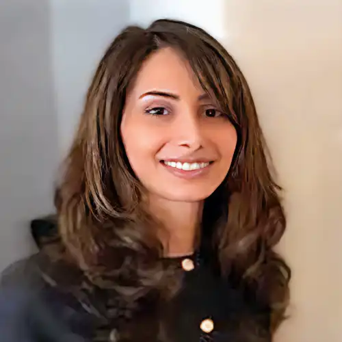 A headshot of Zahra Yarmand standing in front of a tan wall.