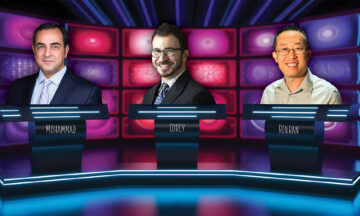 The three new faculty members are standing behind podiums on the set of a game show.