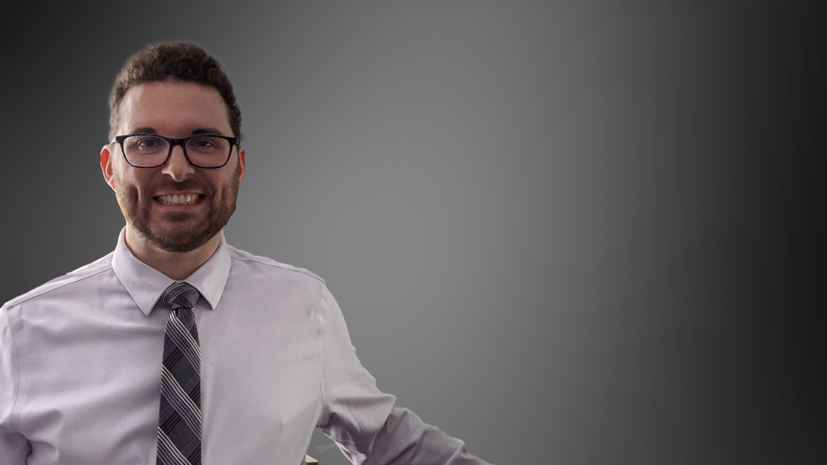 Josh Domeyer is standing Infront of a grey background, smiling into the camera