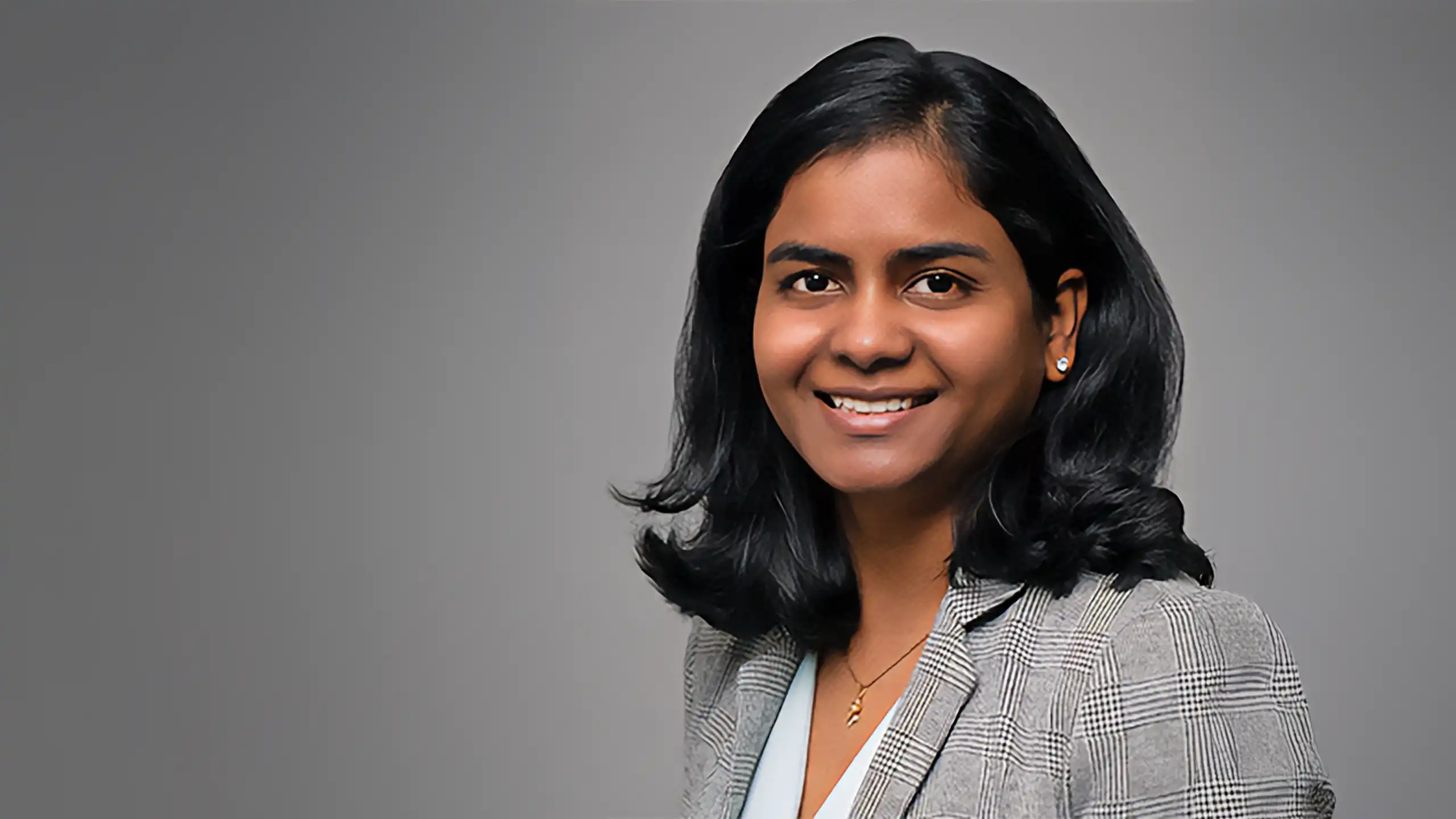 A headshot of Sneha Narra standing in front of a gray background.