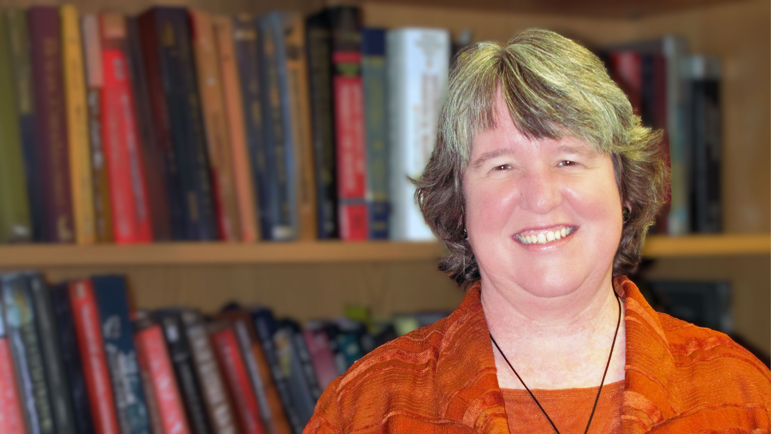 A headshot of Susan Sanchez standing in front of some bookshelves.