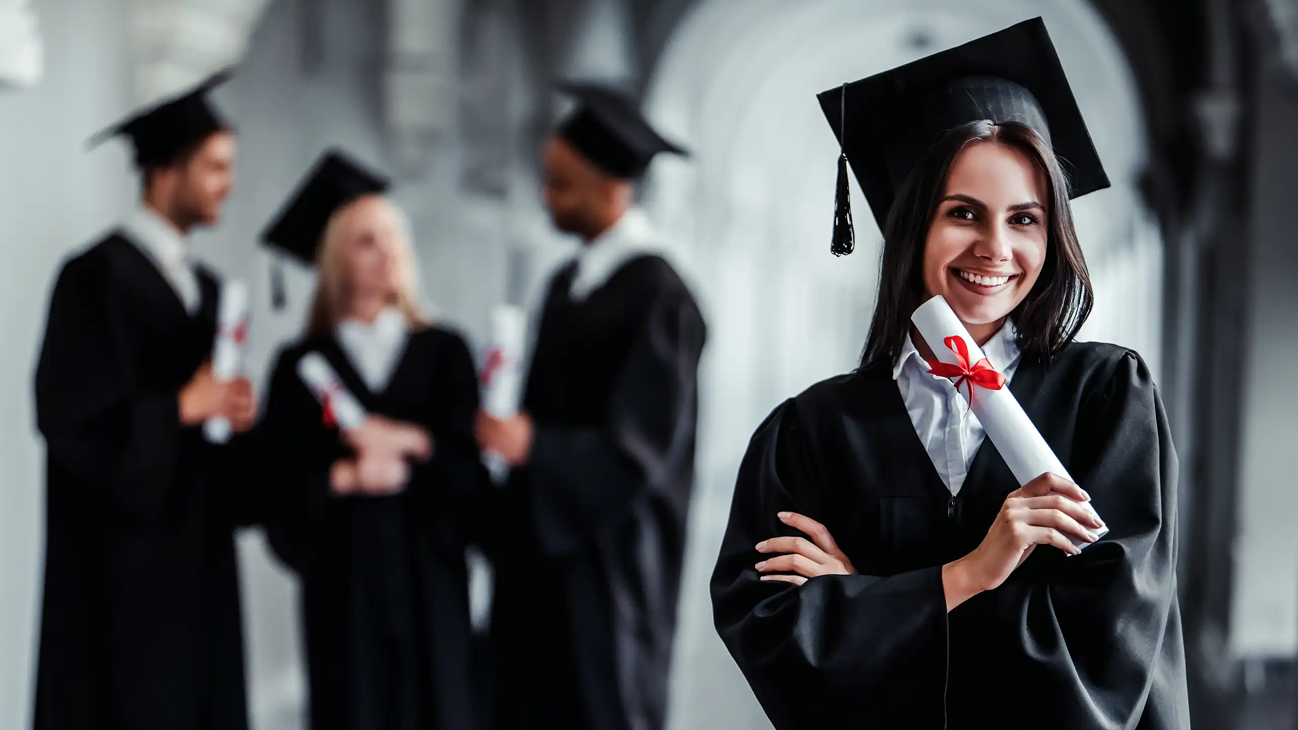 A female student is standing in the hallway of a large building with her arms crossed and holding her degree.