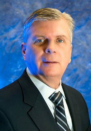 A headshot of Patrick Murray standing in front of a blue marbled background.