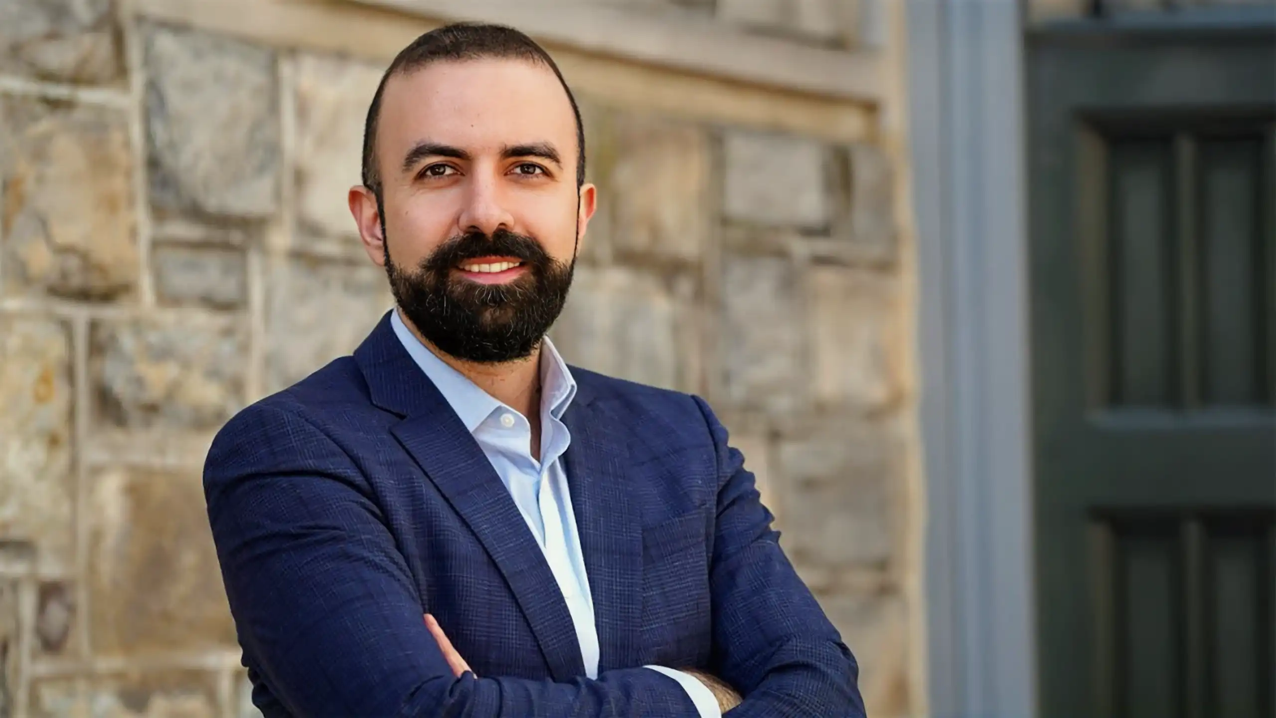 A headshot of Salt Tunc standing in front of an old stone building