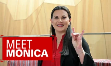 A headshot of Monica Morgan sitting on a couch in Fitts-Woolard Hall showing off her best "Wolfie". Also the words "Meet Monica" on a red background floating to her left.